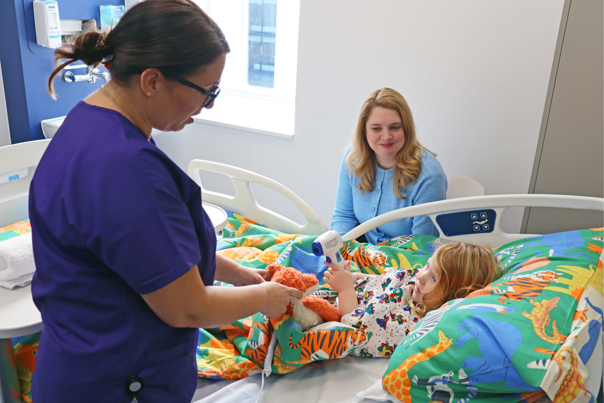 Child in bed in paediatric ward being seen by a nurse